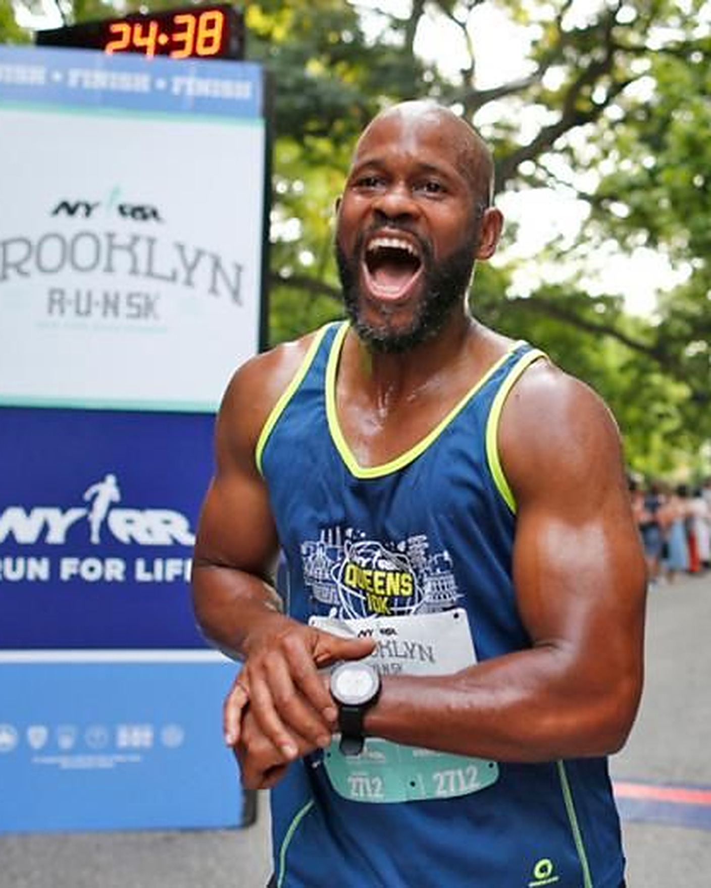 A runner grinning at the finish line of a New York Road Runners 5K, checking his watch
